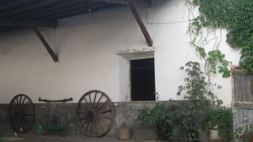 Un edificio rústico con fachada blanca, vigas de madera, una noria grande y plantas en macetas.