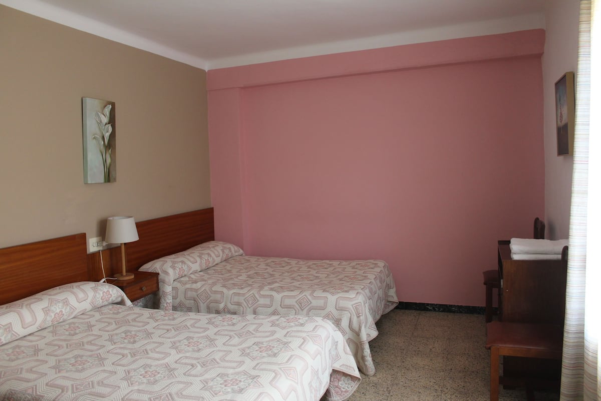 A hotel room with two beds, a wooden headboard, a nightstand with a lamp, a chair, and a wall-mounted painting.