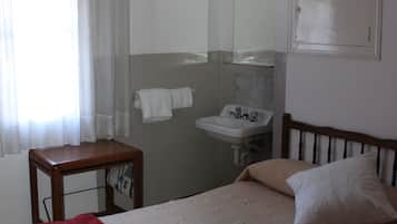 Un dormitorio con cama, mesita de noche, ventana con cortinas, lavabo y espejo.
