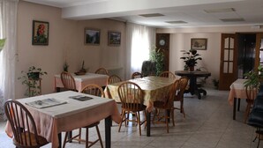 A dining area with multiple tables and chairs, a clock on the wall, and several potted plants. - Pensión Peperillo (Graus)
