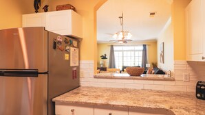 Una cocina con refrigerador de acero inoxidable, gabinetes blancos, encimeras de granito y una araña.