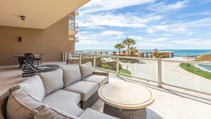 Un balcón con sofá y mesa, con vistas a una piscina y palmeras.