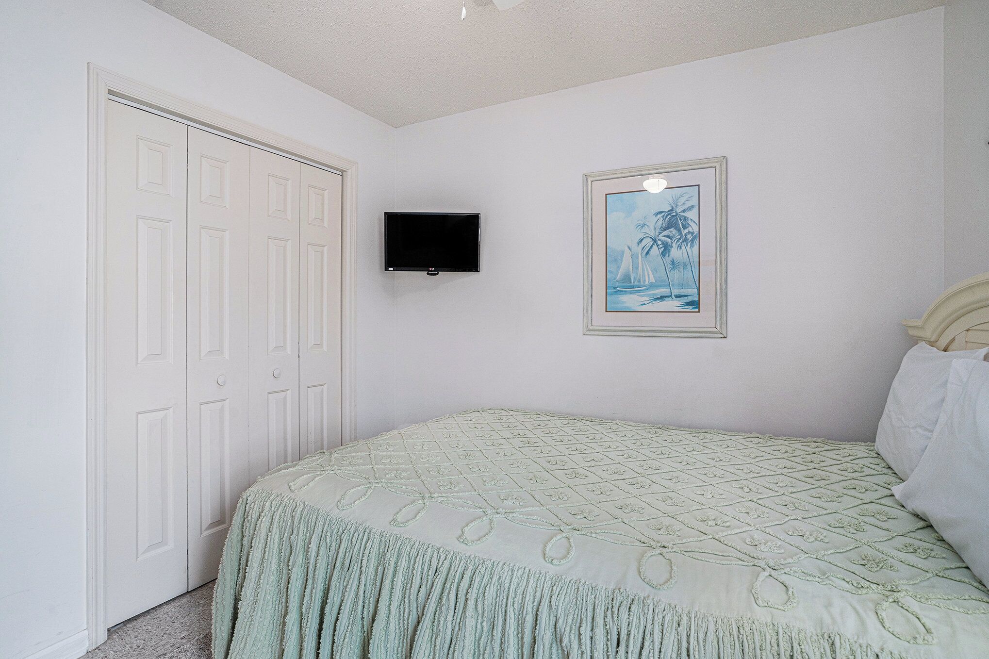 A bedroom with a bed, a television, a framed picture, and a door.