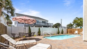 A backyard with a swimming pool, lounge chairs, and a patio table with an umbrella. - The Cotton Patch in Cherry Grove: Walking Distance to Beach! Private Pool! (North Myrtle Beach)