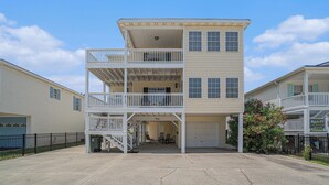 A two-story building with a balcony on the upper floor and a garage on the ground floor. - The Cotton Patch in Cherry Grove: Walking Distance to Beach! Private Pool! (North Myrtle Beach)