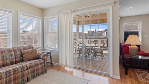 A living room with a plaid sofa, a small table, and a lamp. There is a sliding glass door leading to an outdoor patio with a table and chairs. - The Cotton Patch in Cherry Grove: Walking Distance to Beach! Private Pool! (North Myrtle Beach)