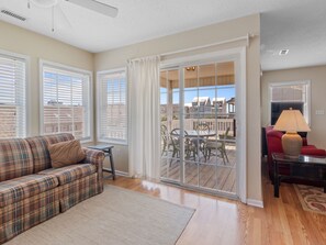 A living room with a plaid sofa, a small table, and a lamp. There is a sliding glass door leading to an outdoor patio with a table and chairs. - The Cotton Patch in Cherry Grove: Walking Distance to Beach! Private Pool! (North Myrtle Beach)
