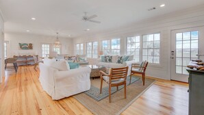 Amplia sala de estar con pisos de madera, muebles blancos y ventanas grandes.