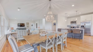 Una cocina amplia con una mesa de comedor de madera, sillas blancas y electrodomésticos modernos.