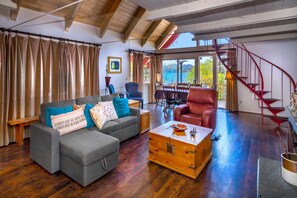 A spacious living room with a grey sofa, ottoman, and a wooden chest. A red spiral staircase is visible in the background. - Lake Arrowhead Lakefront Cabin. Sunset views, swim, beach concerts & outlets! (lake arrowhead)