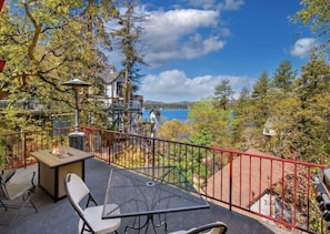 A balcony with a table and chairs, overlooking a lake and trees. - Lake Arrowhead Lakefront Cabin. Sunset views, swim, beach concerts & outlets! (lake arrowhead)