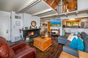 A spacious living room with a fireplace, a dining area, and a kitchen. - Lake Arrowhead Lakefront Cabin. Sunset views, swim, beach concerts & outlets! (lake arrowhead)