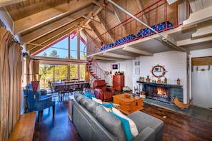 A spacious living room with a high ceiling, a fireplace, and a staircase leading to an upper level. - Lake Arrowhead Lakefront Cabin. Sunset views, swim, beach concerts & outlets! (lake arrowhead)