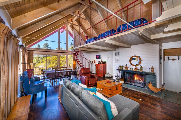 A spacious living room with a high ceiling, a fireplace, and a staircase leading to an upper level.