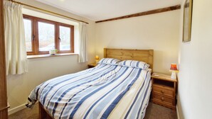 A bedroom with a bed, a window with curtains, a bedside table with a lamp, and a wooden headboard. - The Dairy , Petersfield -  a barn conversion that sleeps 4 guests  in 1 bedroom (Petersfield)