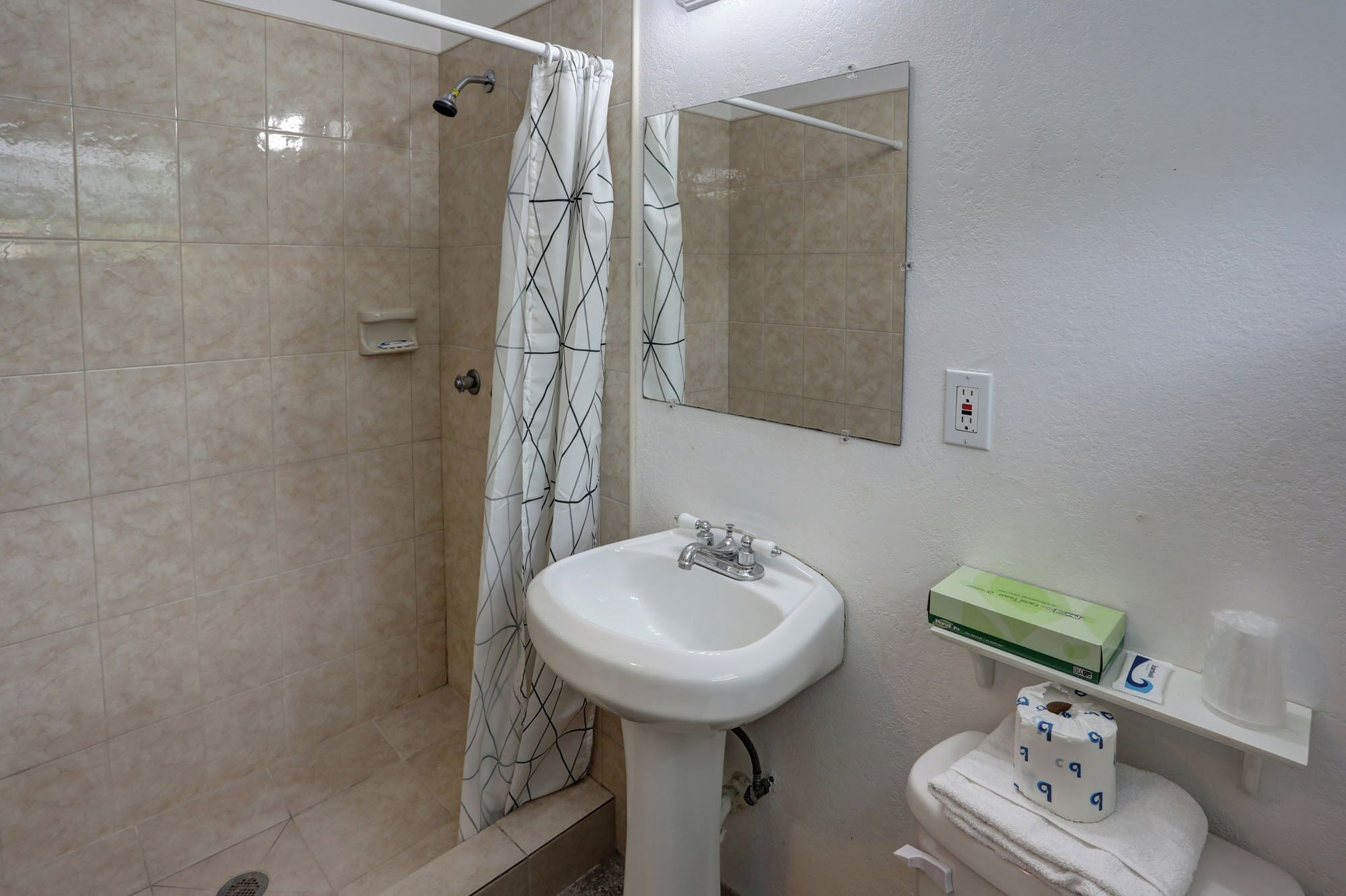 Un baño con ducha, lavabo, inodoro y espejo.