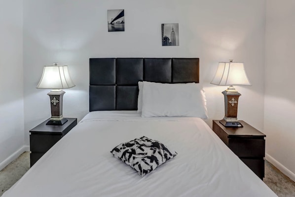 A hotel room with a large bed, two bedside tables with lamps, a headboard, and two wall-mounted pictures.