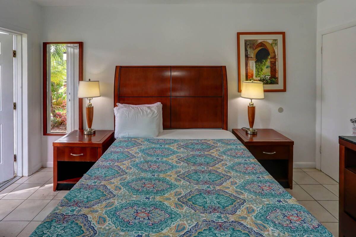 A hotel room with a large bed, two bedside tables with lamps, a wooden headboard, a patterned bedspread, and a framed picture on the wall.