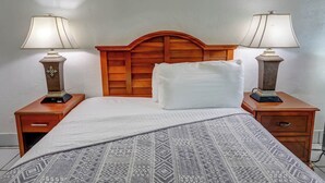 A hotel room with a wooden headboard, two bedside tables with lamps, a bed with a patterned bedspread, and a white pillow. - Green Seas Motel (Hollywood)
