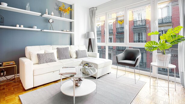 Una sala de estar moderna con un sofá blanco, una mesa de centro redonda y un amplio ventanal con vista a la ciudad.