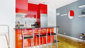 Una cocina moderna con armarios rojos y blancos, un refrigerador de acero inoxidable y una barra con cuatro sillas.