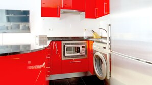 Cocina compacta con armarios rojos, microondas integrado, lavadora y refrigerador de acero inoxidable.