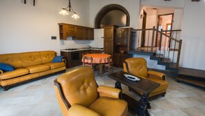 Een ruime woonkamer met een zithoek, een eettafel en een trap naar een verdieping erboven.