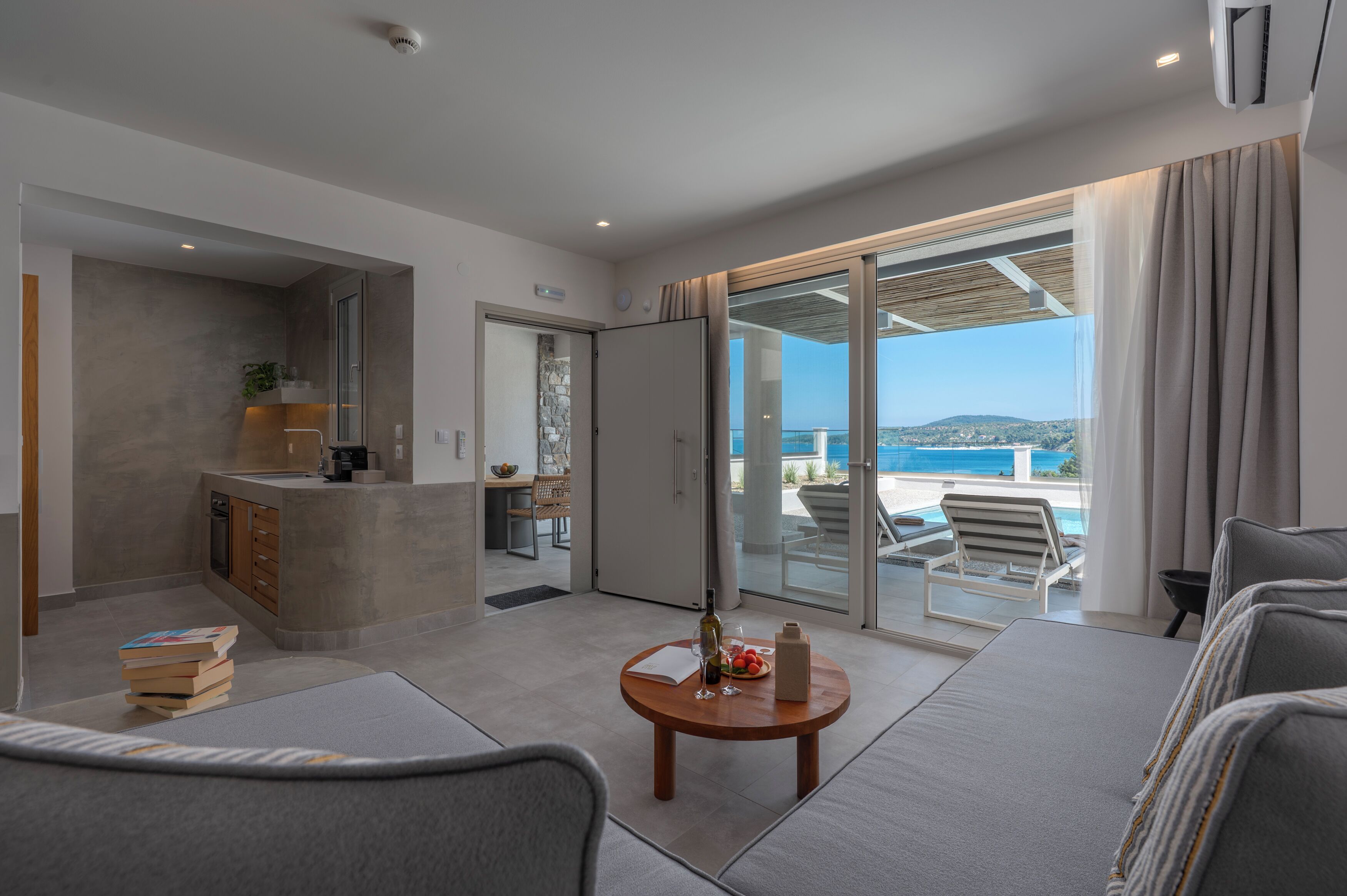 A modern hotel room with a balcony, a dining area, and a view of the sea.