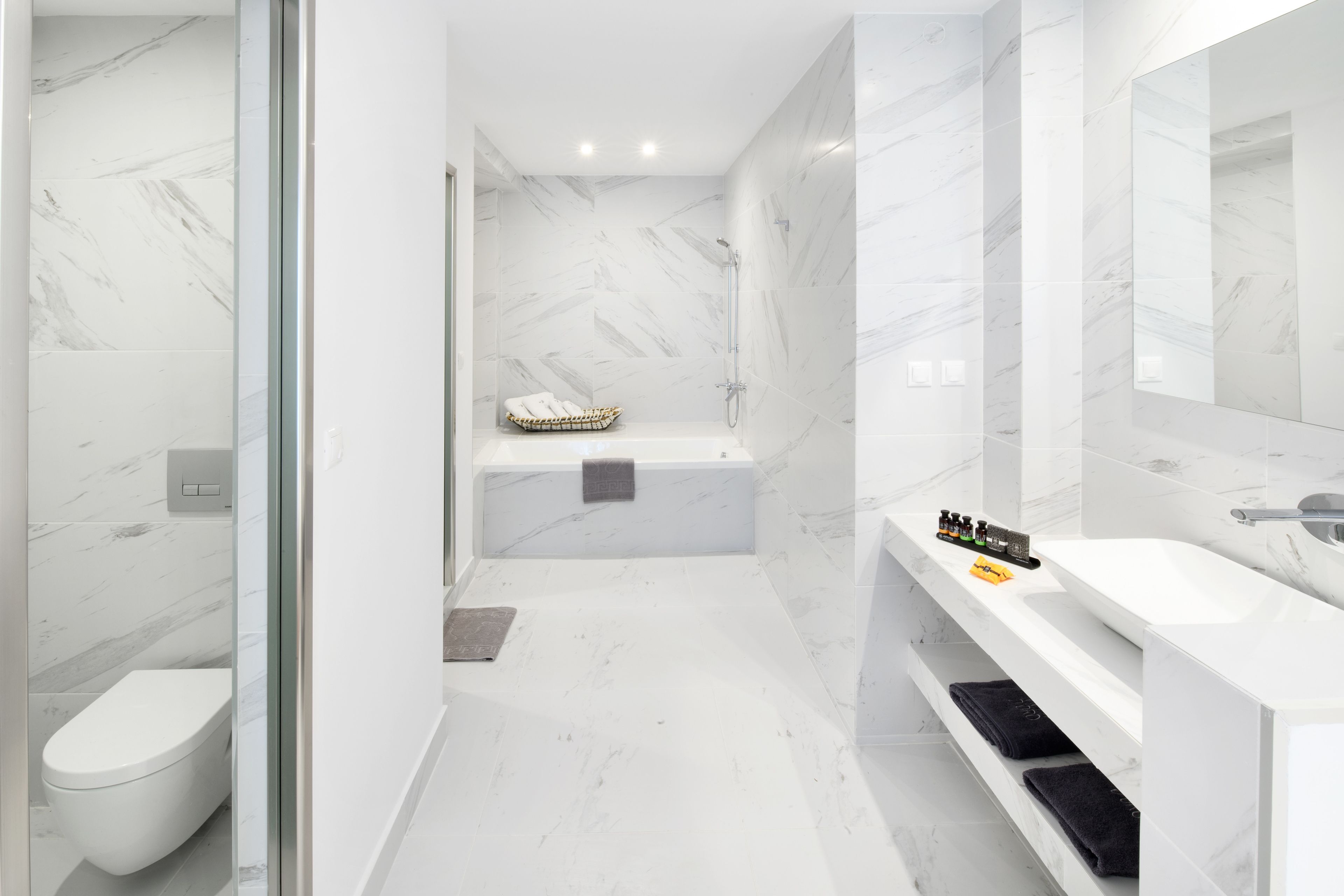 Une salle de bain moderne avec un sol en marbre blanc, une douche en verre, une baignoire blanche et un meuble-lavabo avec un miroir et un évier.