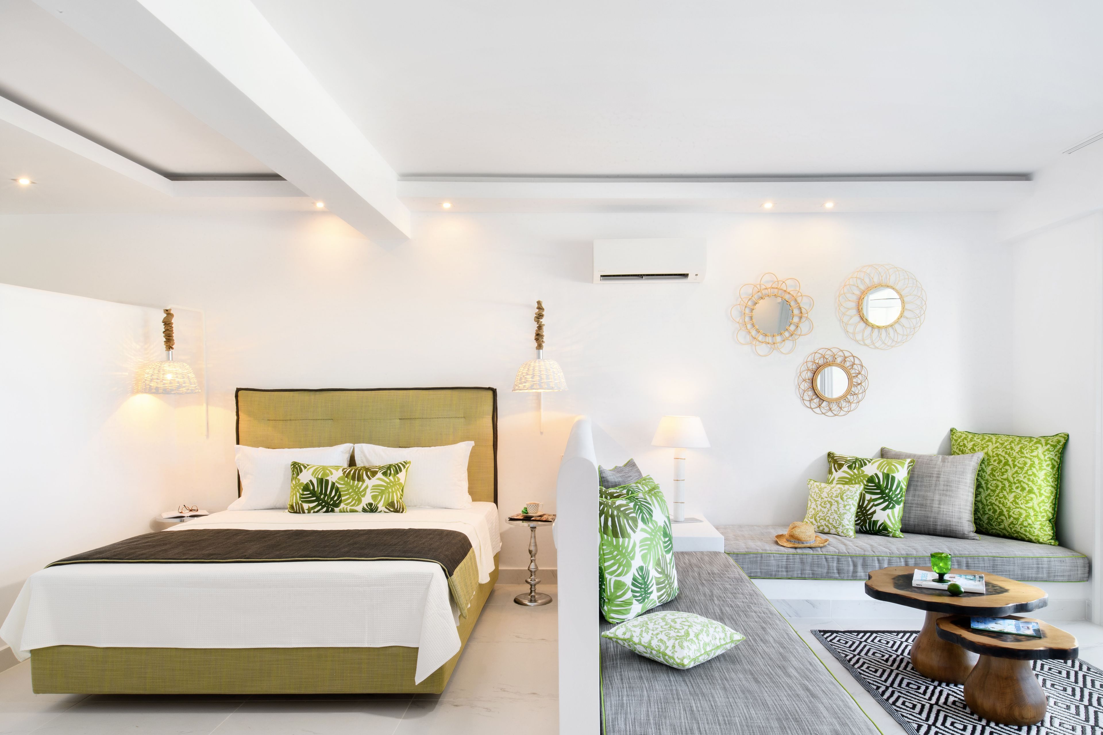 A modern hotel room with a large bed, a sofa, and a small table. There are decorative mirrors and wall sconces.