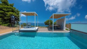 Une piscine d’un bleu éclatant, avec une terrasse en bois, un espace détente et une vue sur la mer.