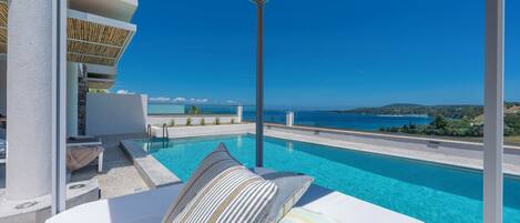 Un área de piscina exterior moderna con vista despejada al mar e piscina infinita blanca.