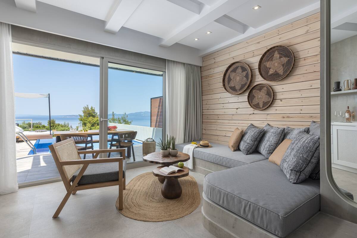 Uma sala de estar moderna com uma janela ampla, um sofá, um espaço para refeições e vista para o mar.