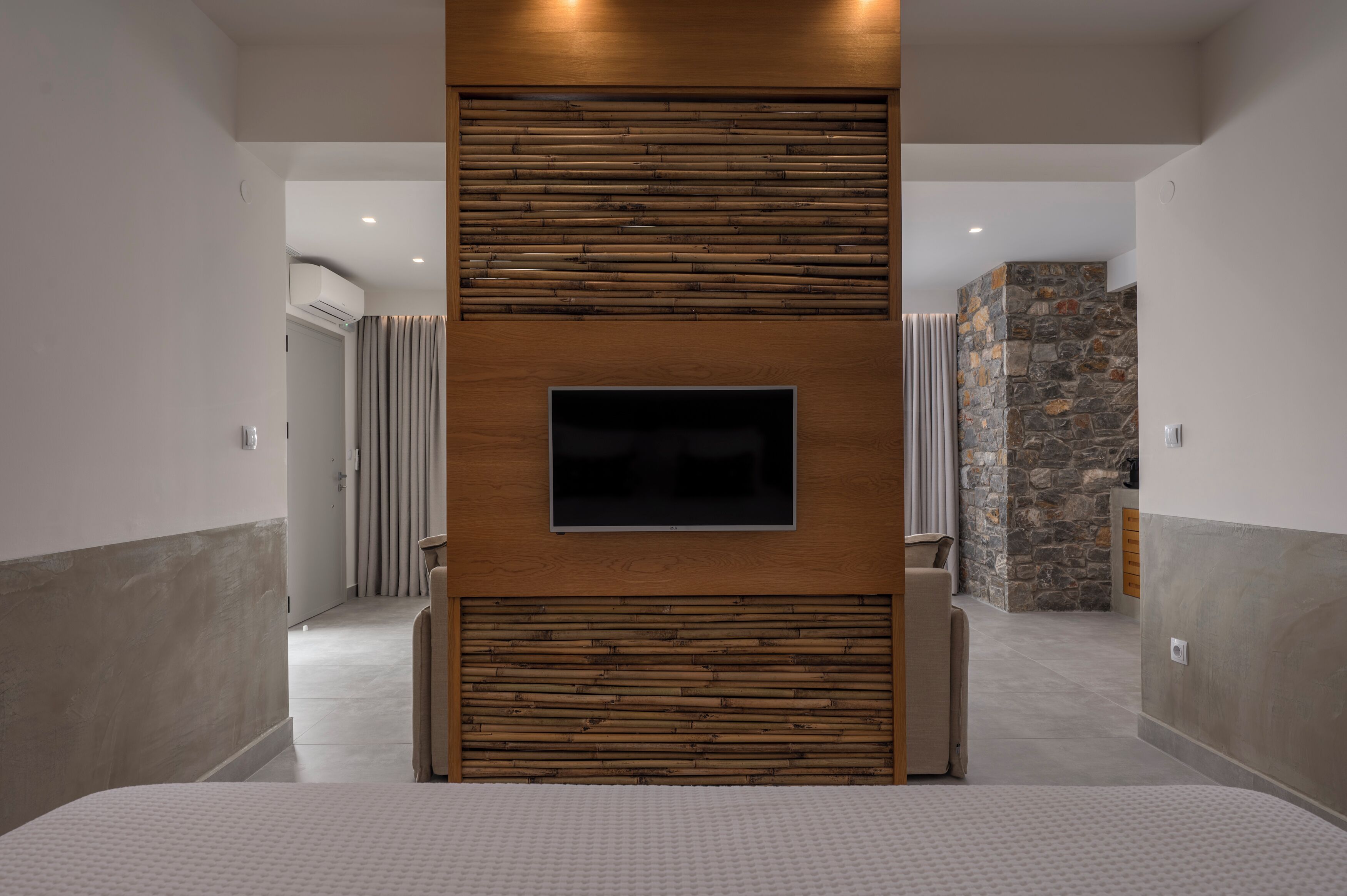 Un pasillo con una televisión de pantalla plana montada en un panel de madera, una pared de acento de piedra y un diseño interior moderno.