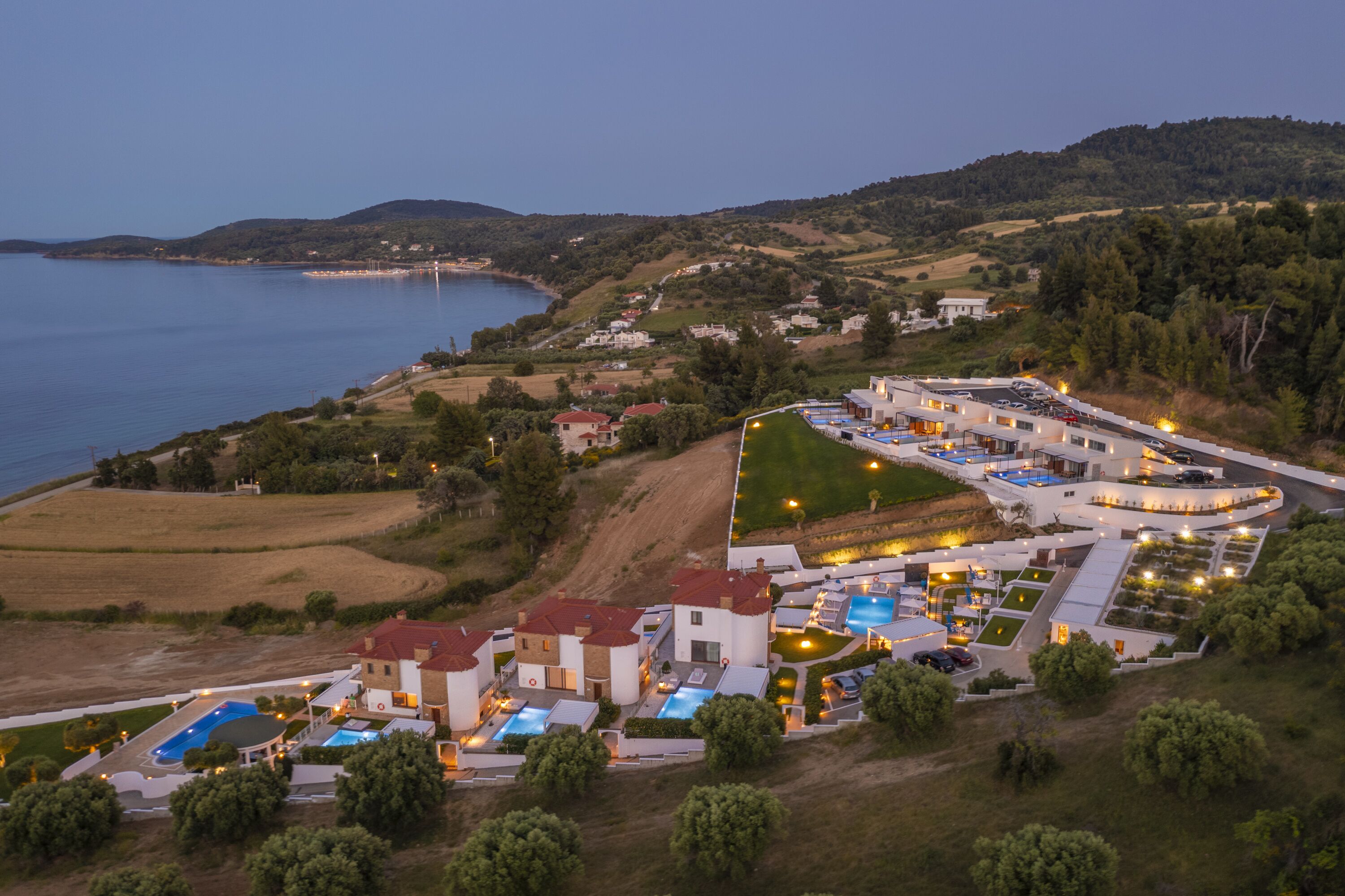 Vista aèria d'una estació turística costanera amb diversos edificis, piscines i un ampli aparcament.