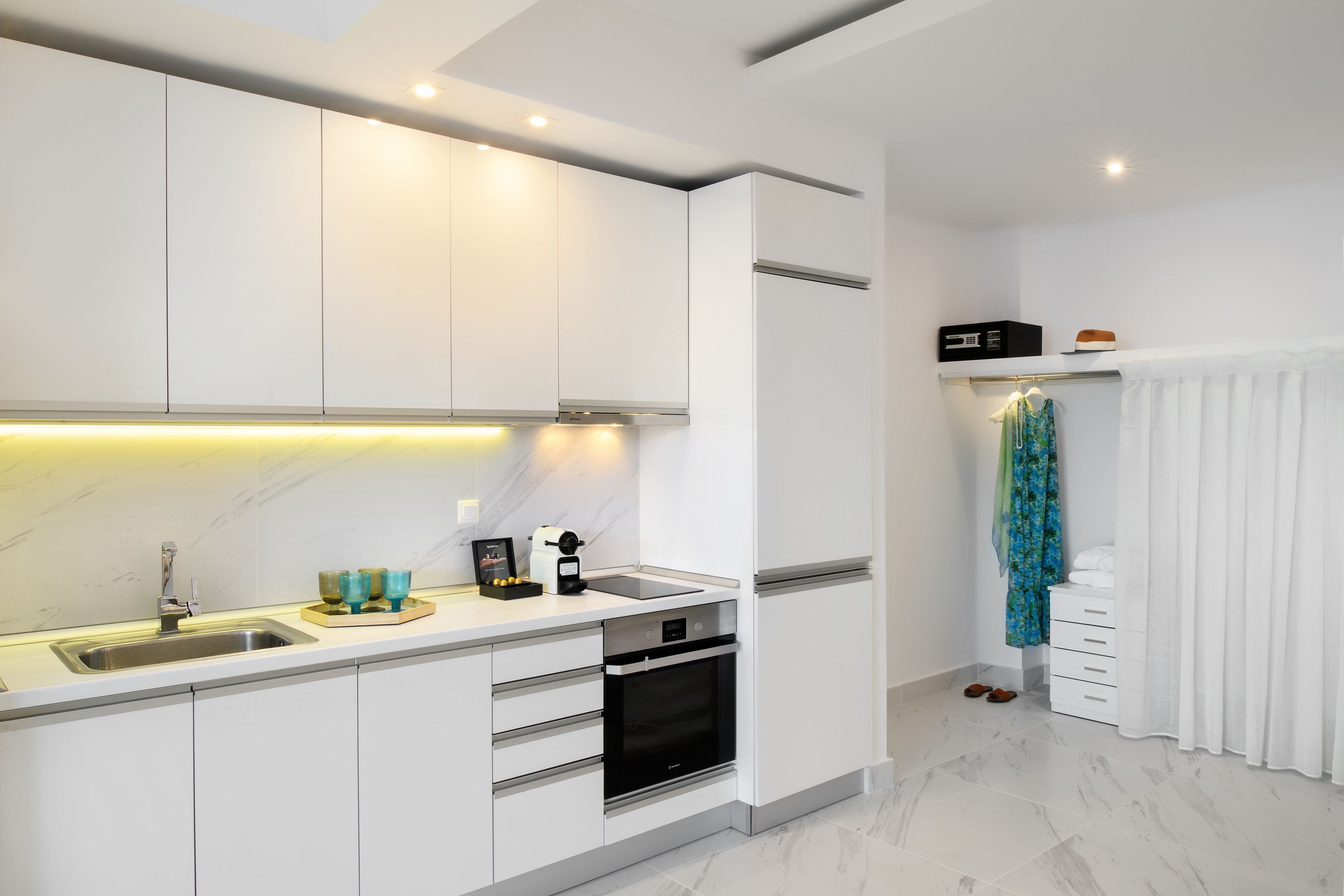 A modern kitchen with white cabinets, a stainless steel sink, and a built-in oven.