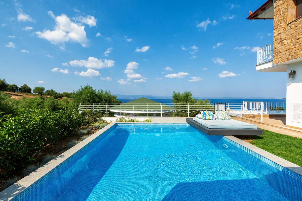 Piscina com vista para o mar, rodeada por vegetação e um edifício de pedra.