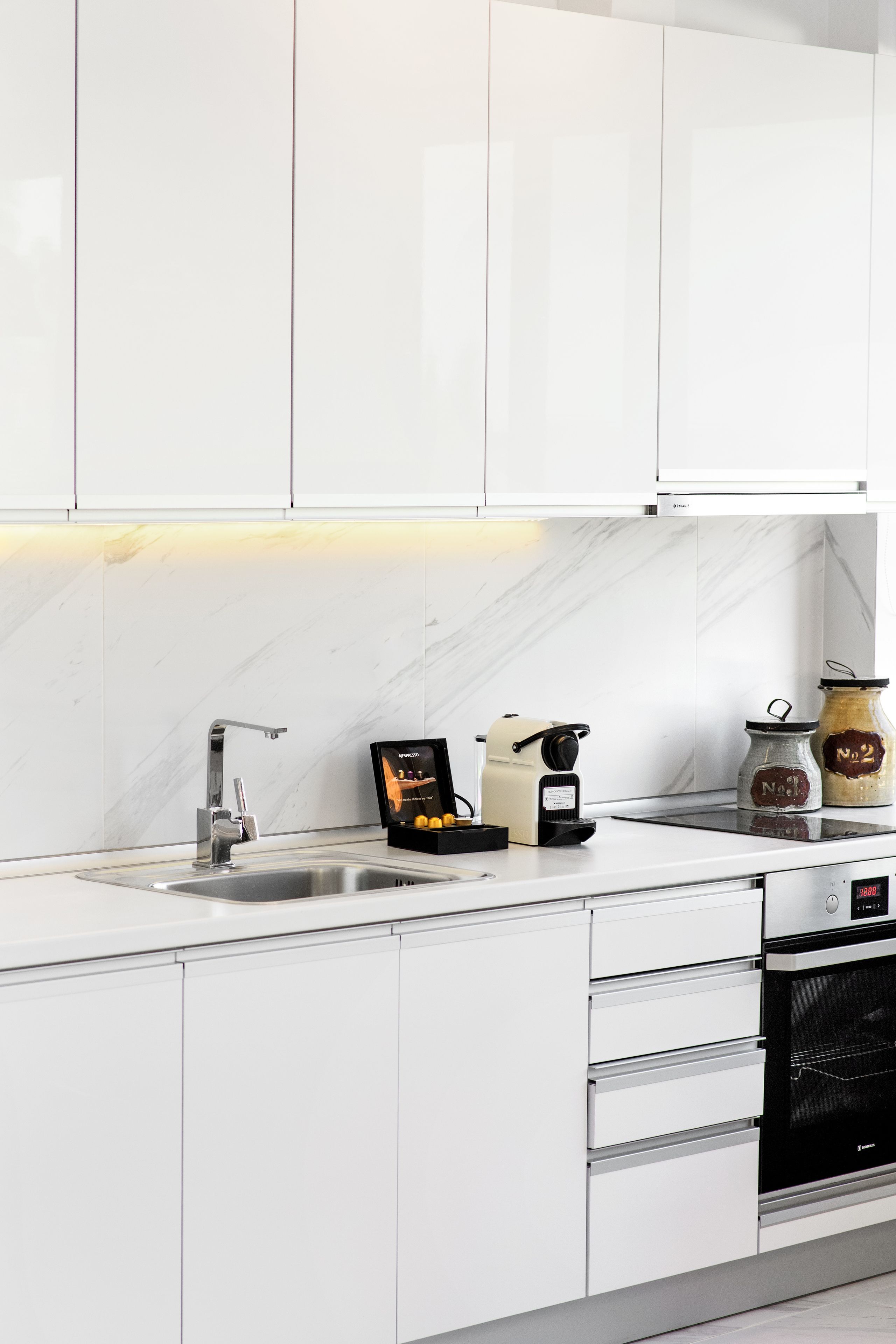 A modern kitchen with white cabinets, a stainless steel sink, a coffee machine, and two jars on the counter.