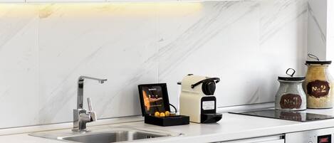 A modern kitchen with white cabinets, a stainless steel sink, a coffee machine, and two jars on the counter.