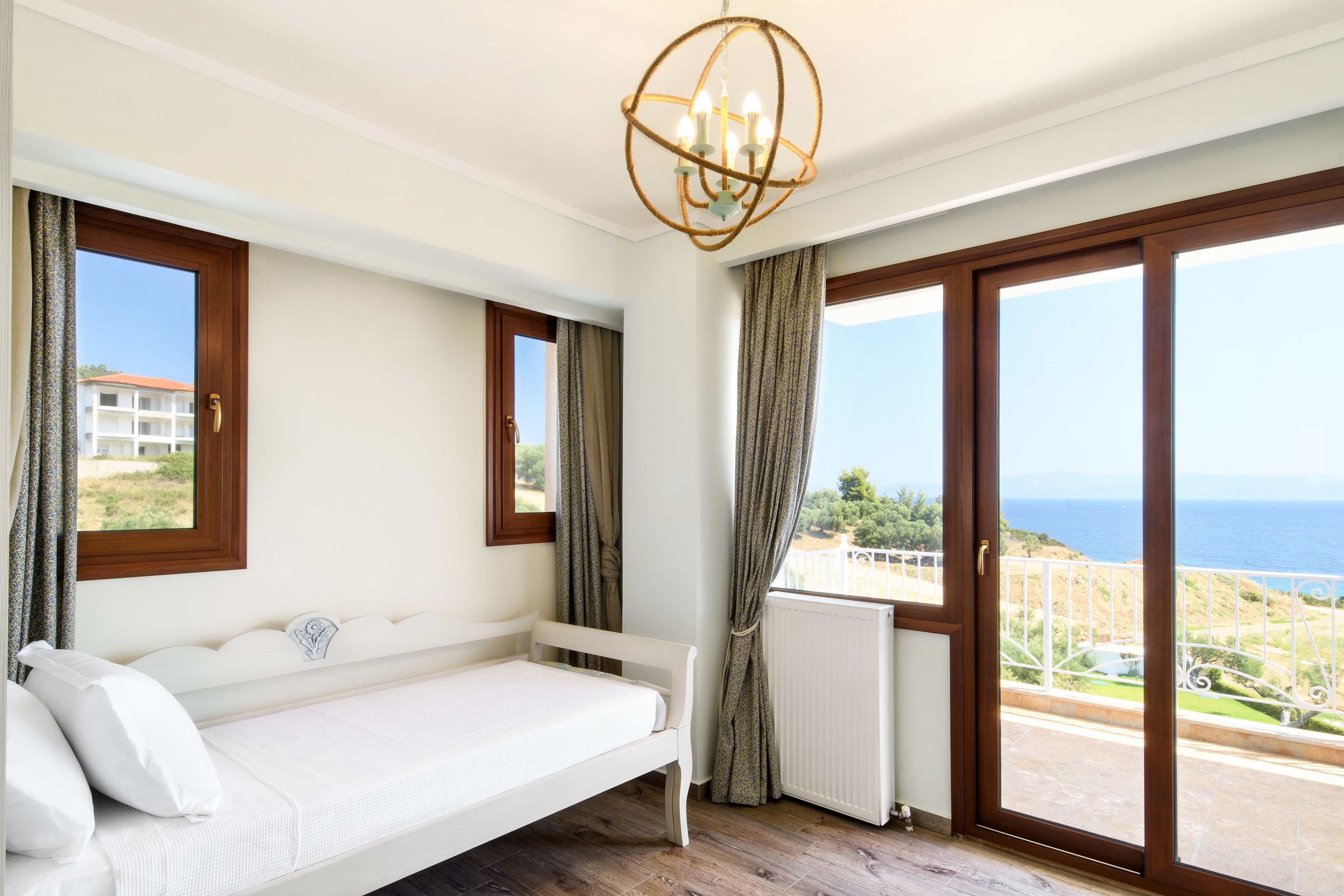 A bedroom with a white bed, large windows, and a view of the sea.