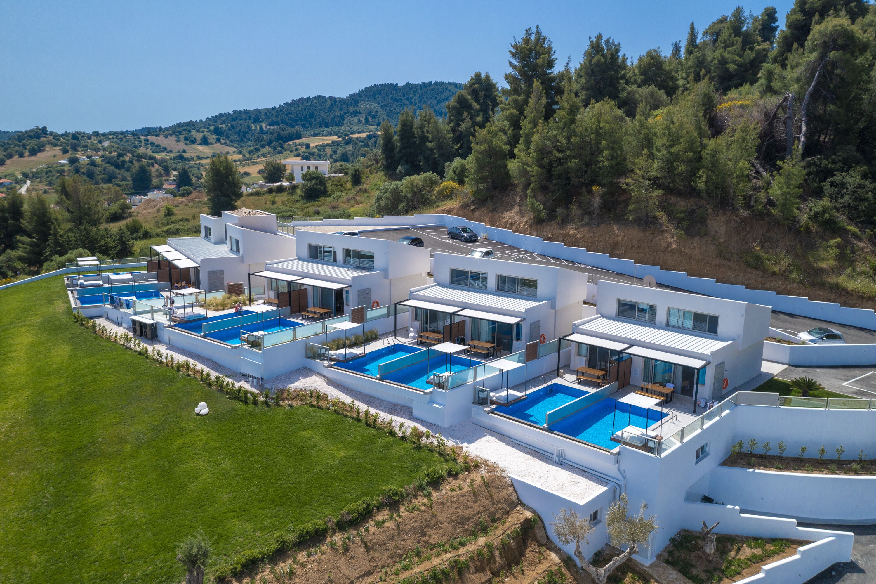 Ein modernes Resort mit mehreren Schwimmpools, weißer Architektur und einer malerischen Hügelkulisse.