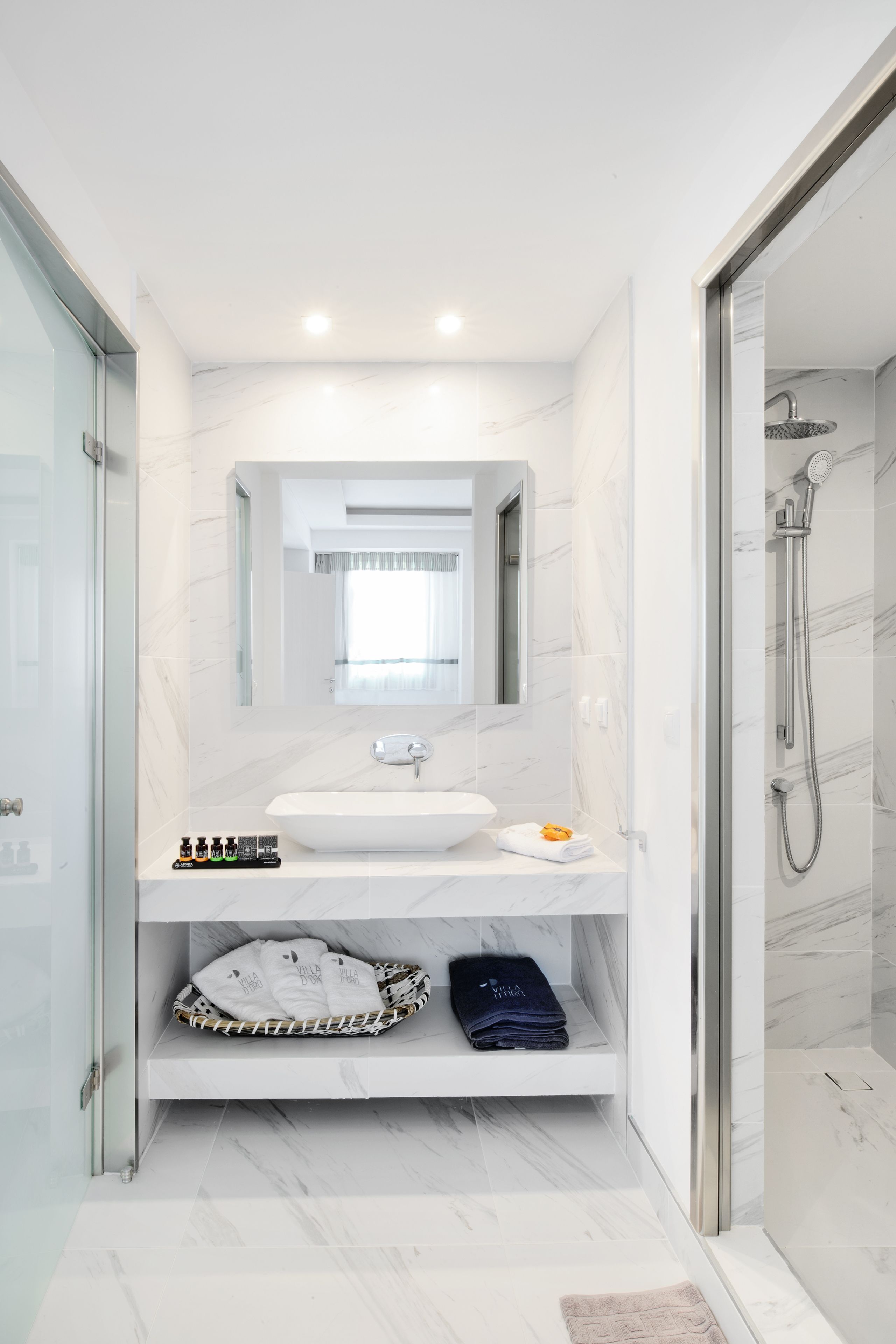 Un baño moderno con un lavamanos blanco, un espejo grande y una ducha con cerramiento de vidrio.