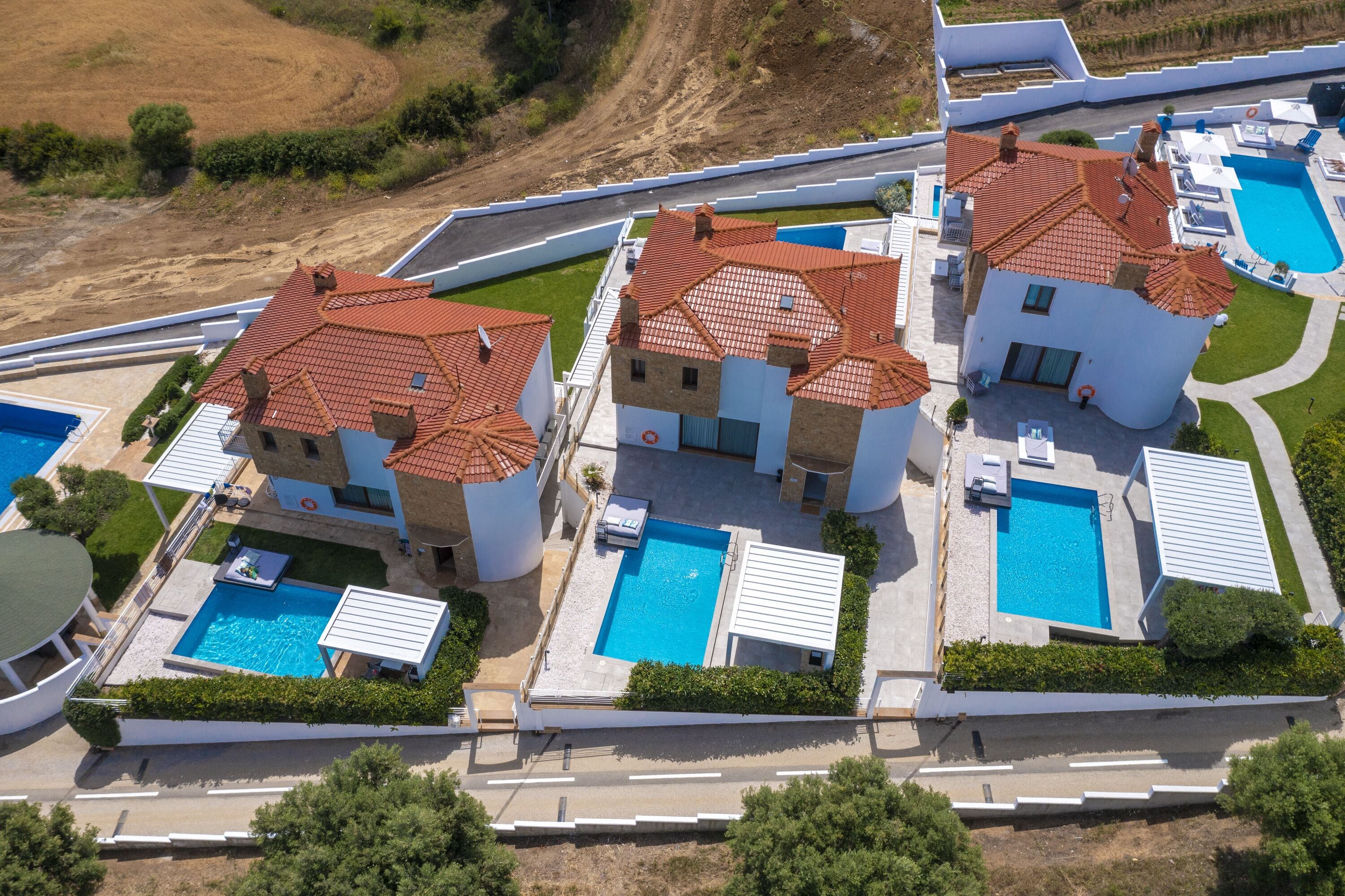 A residential area with multiple houses, each with a swimming pool and a tiled roof.