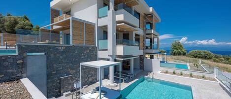 Un edificio moderno de varios pisos con piscina, zona de estar exterior y vista al mar.