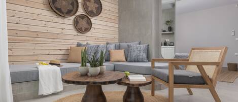 A modern living room with a grey sofa, wooden coffee table, and a wooden chair. There are two woven baskets on the wall and a large mirror.