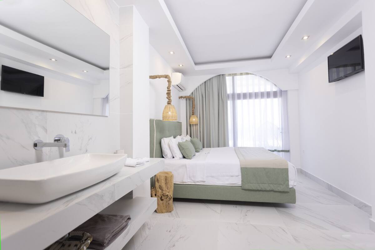 Quarto moderno com uma cama grande, uma toucador com pia de mármore e uma televisão de tela plana fixada na parede.