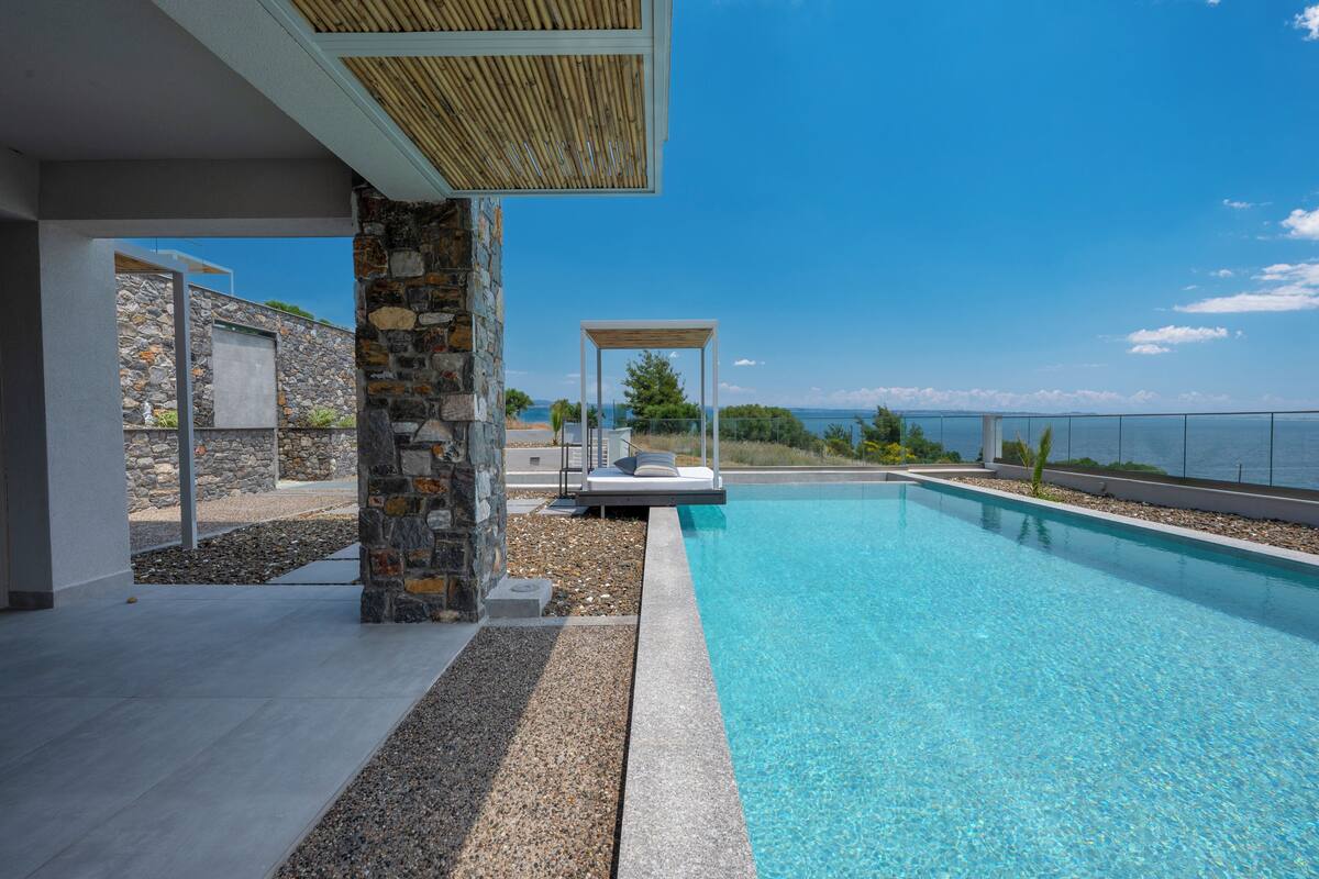 Uma piscina moderna ao ar livre, com parede de pedra e vista para o mar.