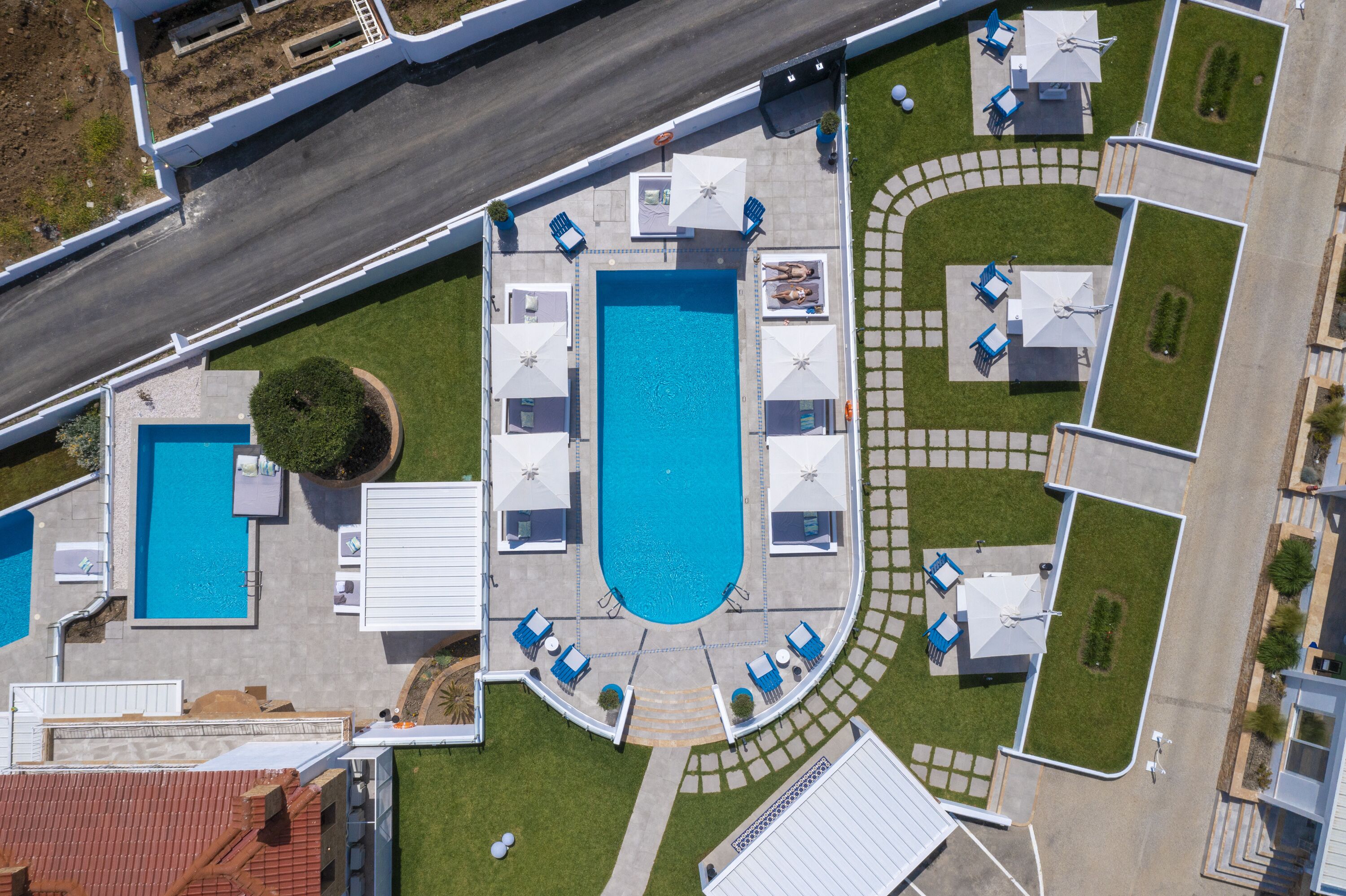 Eine Vogelperspektive zeigt ein Hotel mit einem zentral gelegenen Schwimmbad, mehreren Loungebereichen und einem gepflegten Rasen.