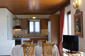 A kitchen with wooden cabinets, a tiled backsplash, a dining table with chairs, and a television on a stand.