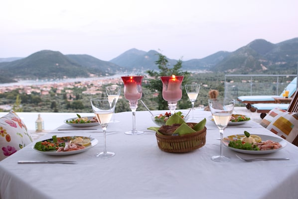 A table set with plates of food, glasses of wine, and candles, overlooking a scenic view of mountains and a town.